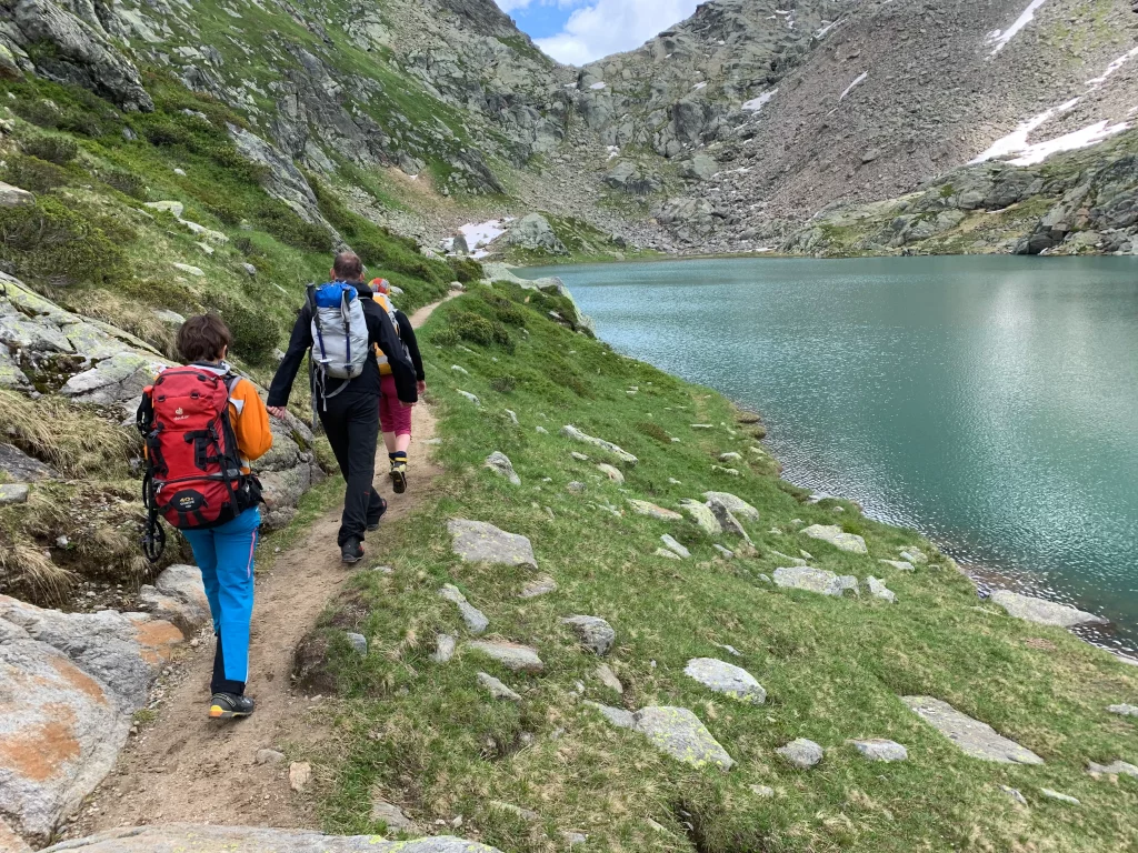 Gruppe wandert in den Tessiner Bergen auf einem schmalen Pfad an einem See entlang