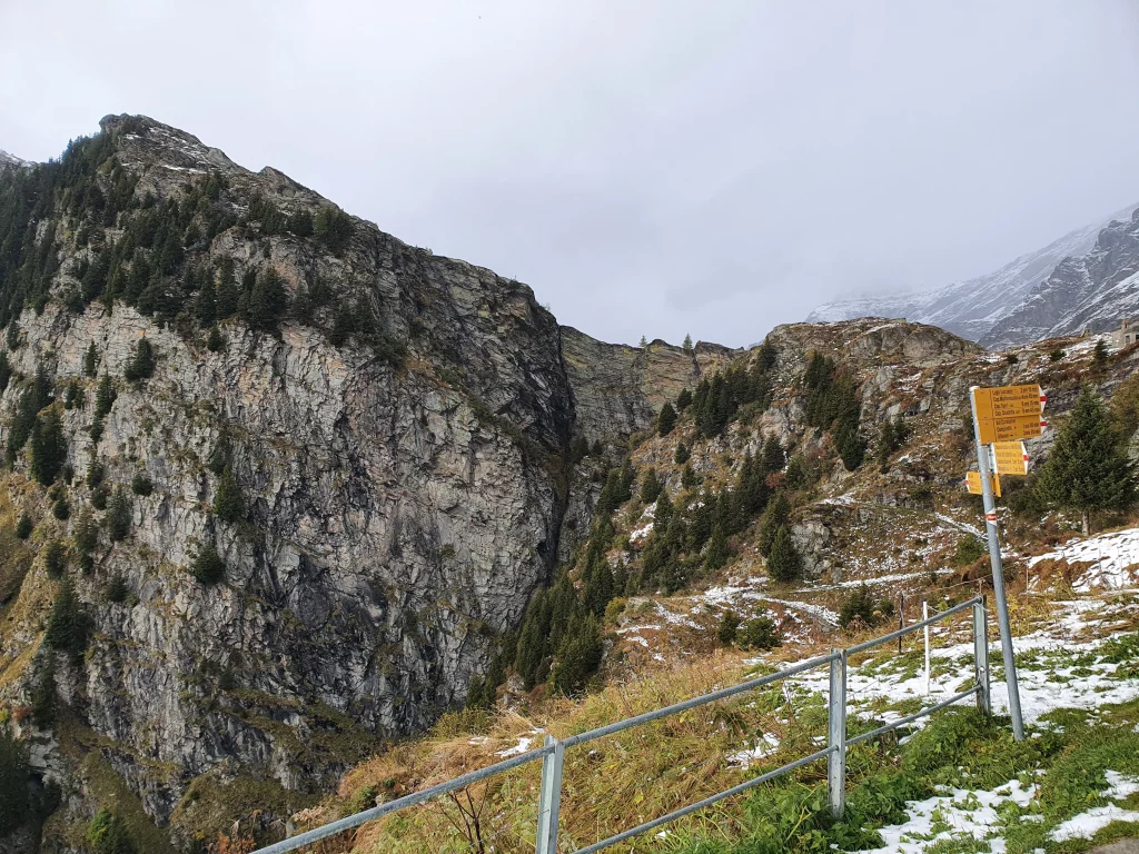 Gelber Wegweiser vor Bergmassiv. Im Hintergrund schneebedeckte Berge.